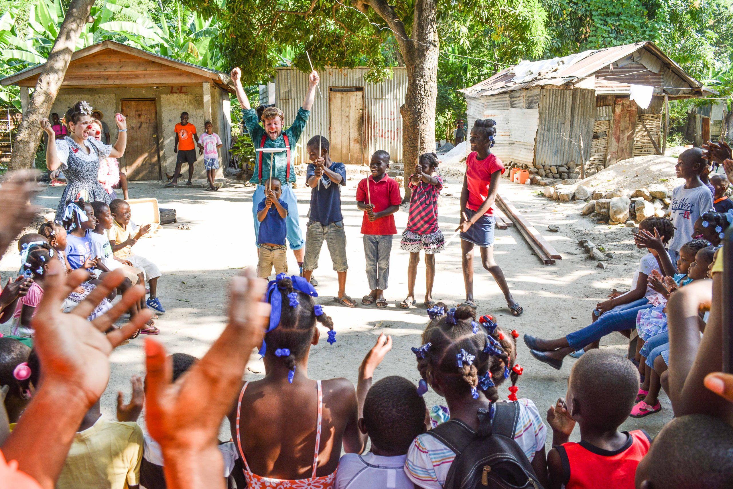 kids putting on a performance under the supervision of a clown by balancing a plate on a stick