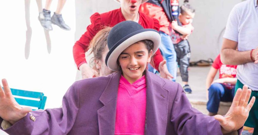 Girl dressed in oversized clothes and bowling hat performs with clowns