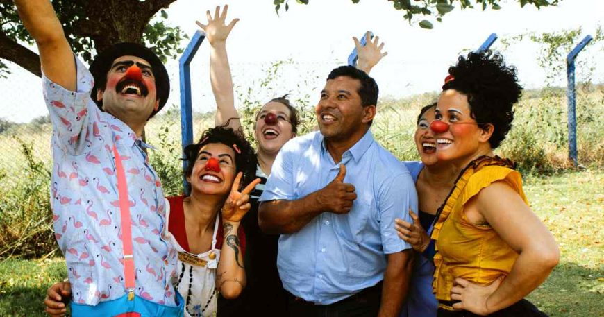 Clowns gather around a non-clown man as they all celebrate with smiles.