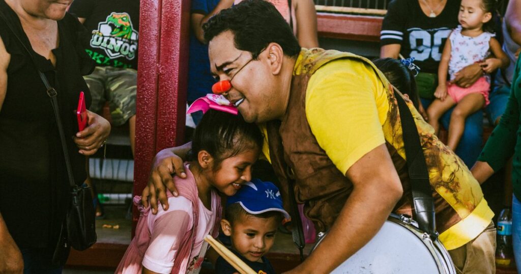 A clown hugs a small boy and girl after a clown show.