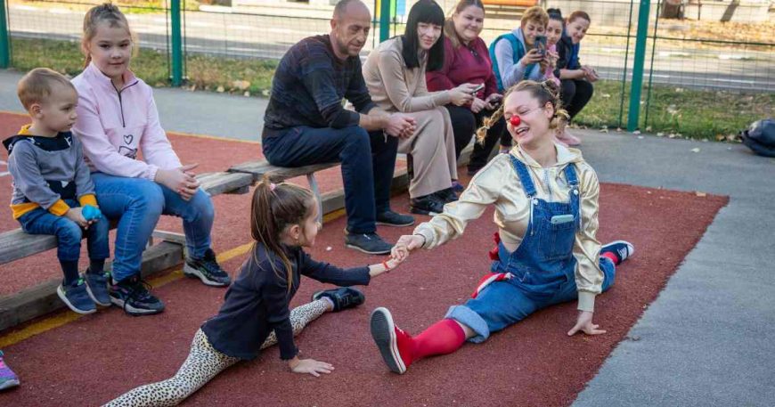 A clown and a child hold hands and do splits together.