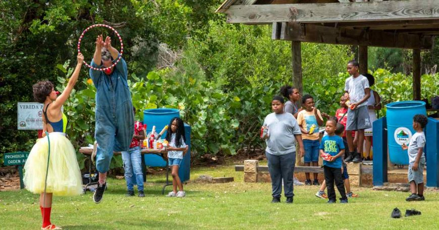 In Puerto Rico, a clown in a dress holds a hoop for a clown in a jumpsuit attempting to jump through.